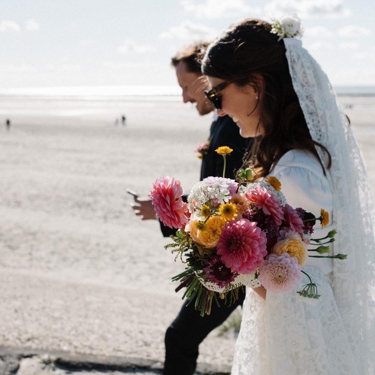 Une mariée avec un bouquet coloré marche sur la plage, accompagnée de son époux. La photo de mariage