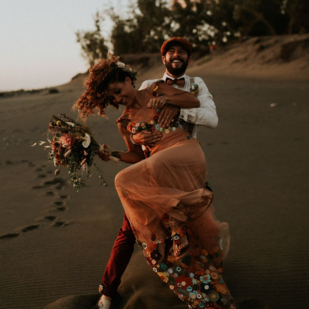 Un couple heureux sur la plage, elle en robe légère, tenant un bouquet, dansent ensemble.