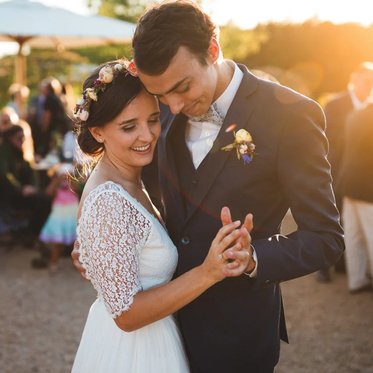 Un couple danse lors d'un mariage en extérieur, entouré d'invités et de lumière dorée.